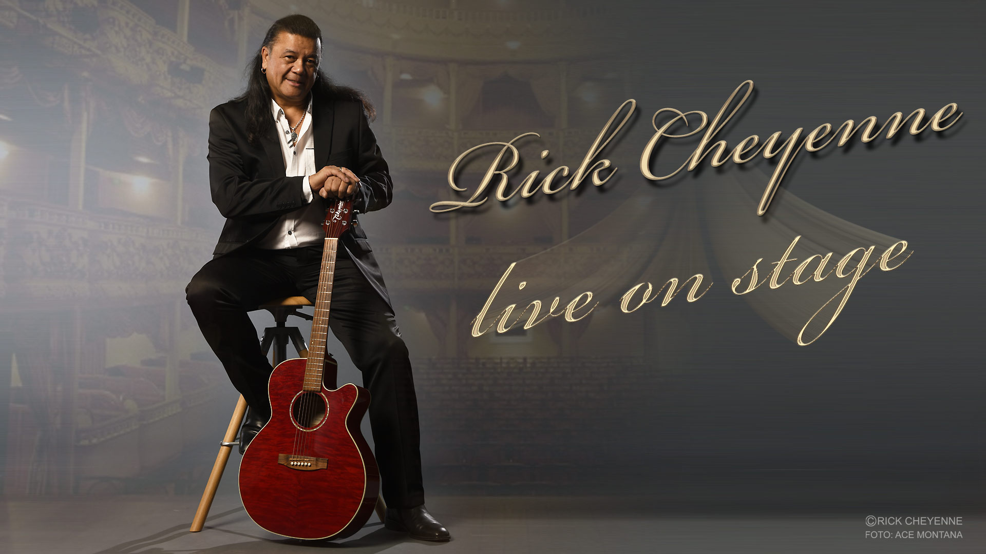 Rick Cheyenne sitzt im dunklen Anzug und weißem Hemd auf einem Hocker und stützt seine Hände auf die vor ihm abgestellte Gitarre. Im Hintergrund sind schwach Balkone eines Theatersaals zu erkennen.