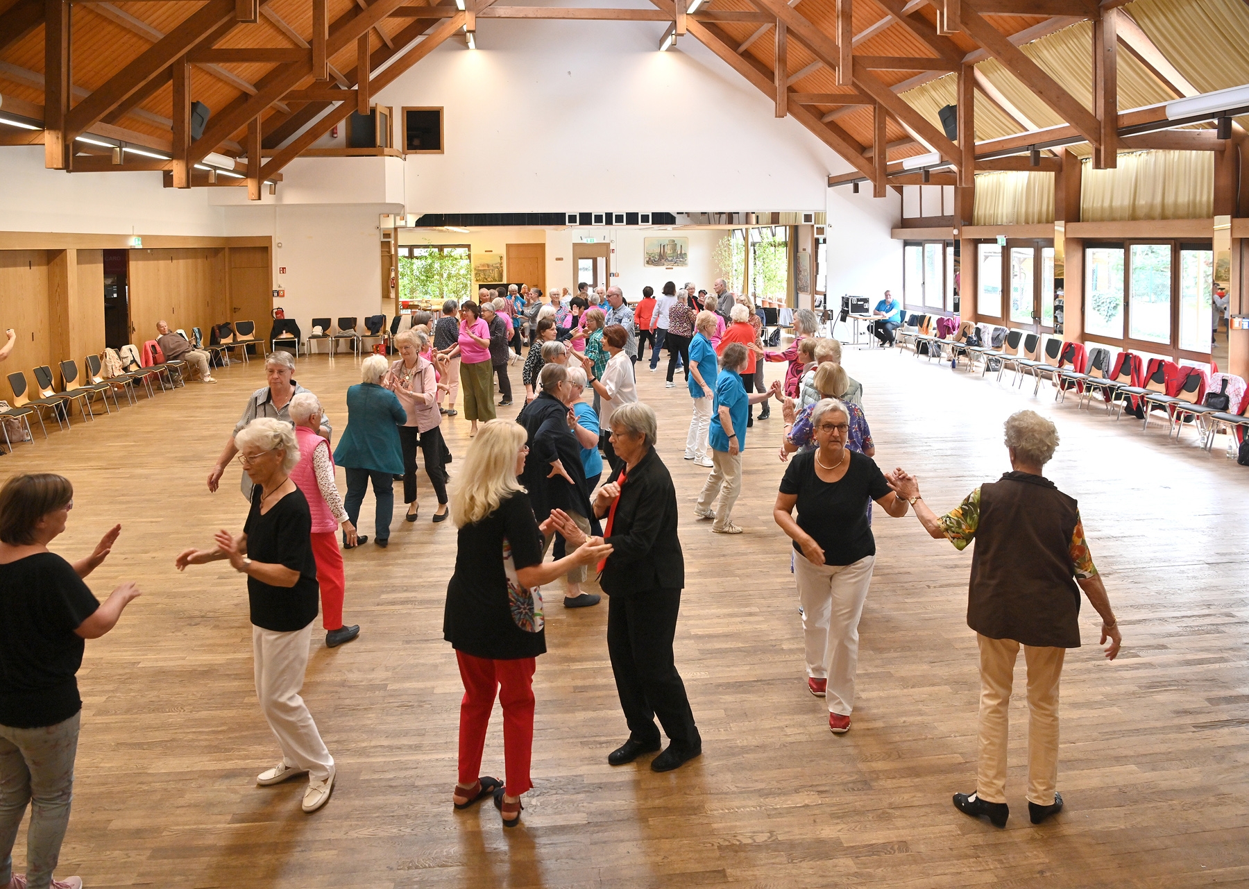 Senioren, die miteinander in einem großem Saal tanzen.