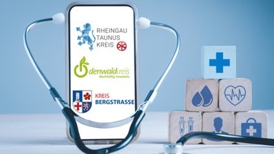 Ein Stethoskop steht vor einem Handy. Rechts davon liegen gestapelt 6 Würfel mit folgenden Symbolen: Arztkoffer, Herz mit Herztönen, Kreuz, zwei Spritzen, zwei Tropfen u nd einem Mann.