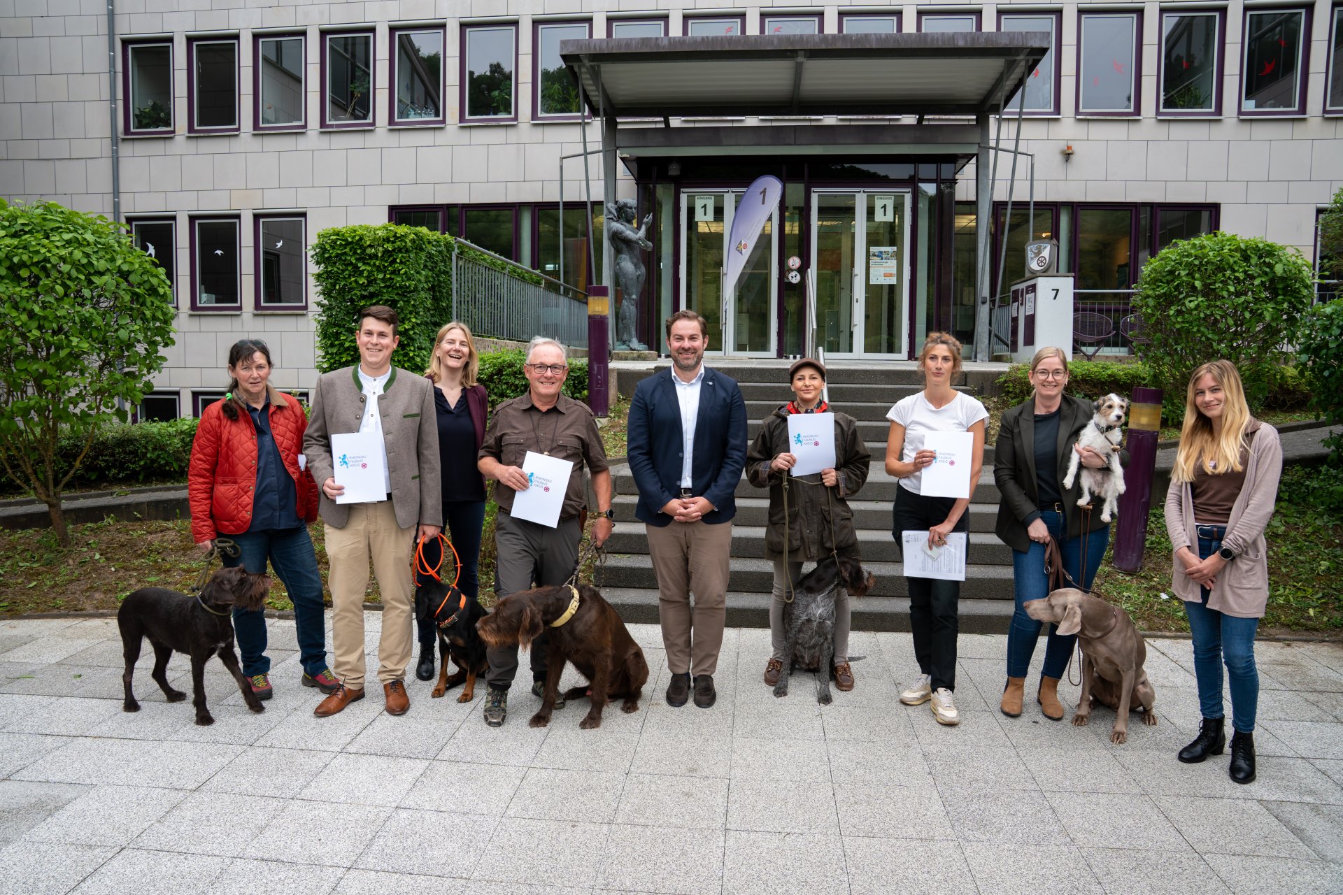 Gruppe von Frauen und Männern mit ihren Hunden vor einem Haus