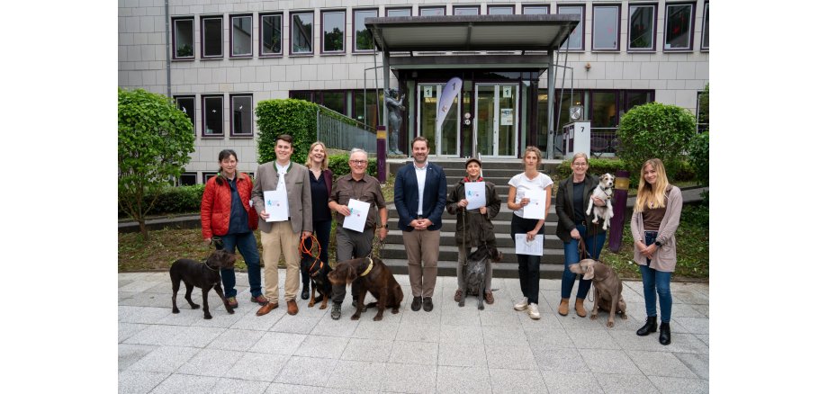 Gruppe von Frauen und Männern mit ihren Hunden vor einem Haus