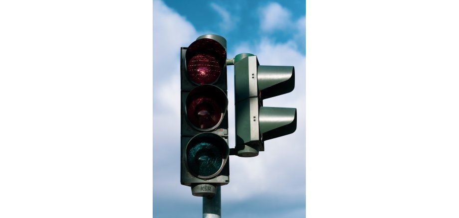 Vor einem blauem Himmel mit weißen Wolken ist eine Ampel, die rot leuchtet. Rechts an der Seite ist die Fußgängerampel mit Blende zu erkennen.