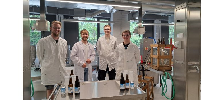 Angehende Fruchtsafttechniker und Winzer an den Beruflichen Schulen Rheingau in Geisenheim. Vier junge Männer stehen in weißen Kitteln in einem Labor. Vor ihnen ein Tisch mit Bechern, Flaschen und Getränkedosen.