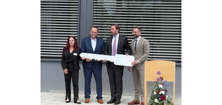 (v.l.n.r.): Karin Daiß (Abteilungsleiterin für die Berufsschule (Duale Ausbildung) und Maßnahmen wie Intea, Werkstätten für Menschen mit Beeinträchtigungen und Kooperationen), Schulleiter BSR Martin Gehlert, Landrat Sandro Zehner und Bürgermeister Christian Aßmann (Geisenheim). Landrat, Schulleiter, Bürgermeister und Abteilungsleiterin halten einen großen Schlüssel in der Hand, im Hintergrund ist die Schule