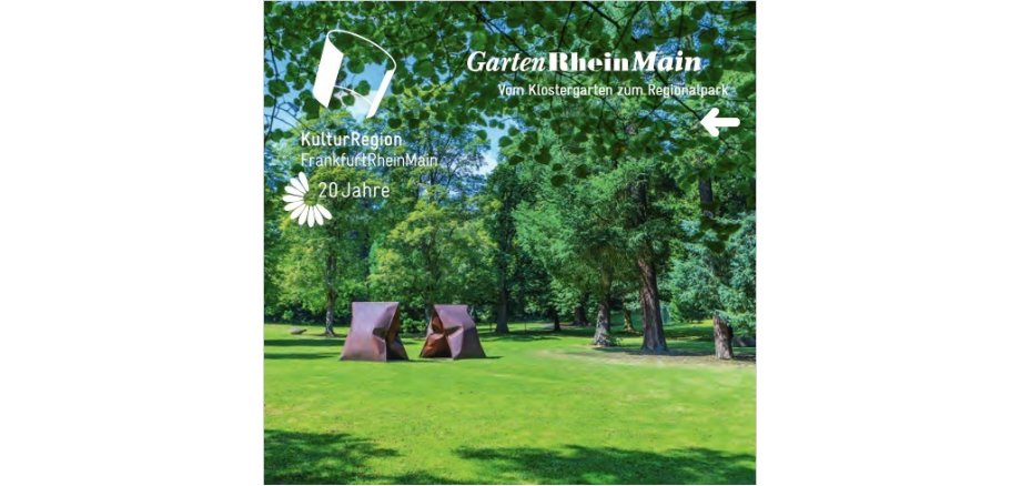 Auf einer Wiese stehen mehrere große, alte grüne Laubbäume und zwei rechteckige braungefleckte Skulpturen, die wie ein aufgestelltes V aussehen.