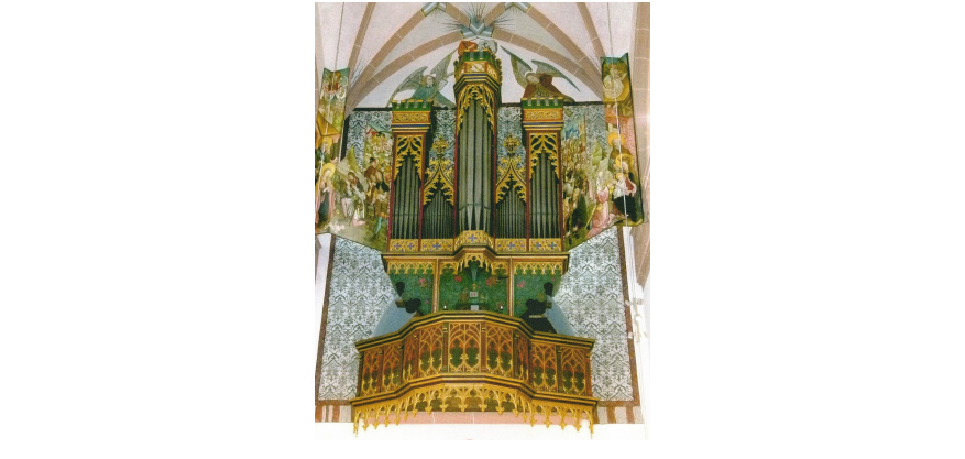 Eine Orgel mit mehreren Orgelpfeifen, die in fünf Rechtecken angeordnet sind, die mit goldenene Ornamenten verziert sind. Das Emporengeländer ist gold, grün und orange-braun dargestellt mit Ornamenten. HInter der Orgel sind auf weißem Untegrund graue Ornamente und neben und oberhalb der Orgelpfeifen sind Personen und Engel gemalt.