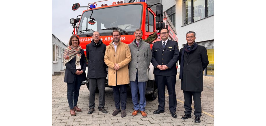 Vor einem Feuerwehrauto stehen vier Männer und eine Frau im Halbkreis. Alle tragen Winterjacken.
