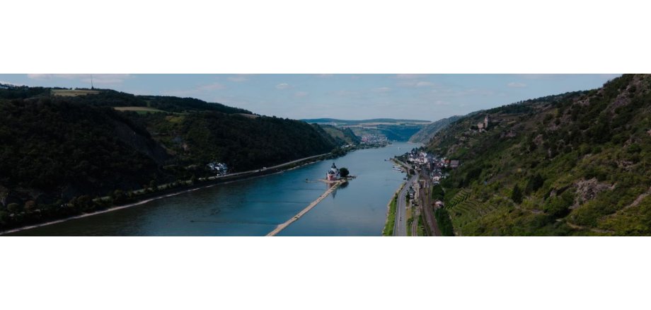 Blick auf das Rheintal und dem Rhein mit den Hängen links und rechts mit Wäldern, Weinbergen, Feldern, Burgen und im Rhein eine weitere Burg und einer langen Sandbank und Anlegern und eine Fähre. Der Himmel ist etwas bewölkt.