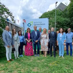 Sechs Männer und sechs Frauen stehen vor einem Schild mit der Aufschrift "Hochschule Geisenheim" auf einer Wiese. Im Hintergrund sind grüne Laubbäume und ein Gebäude mit Flachdach.