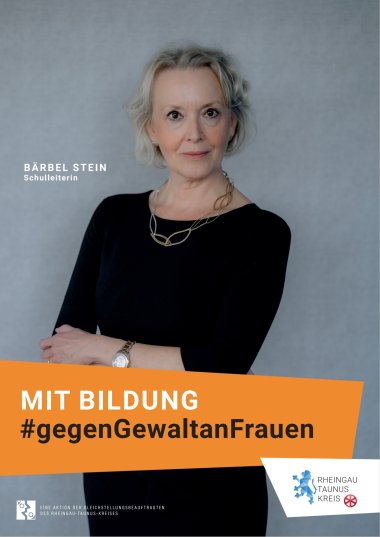 Vor einem grauen Hintergrund steht eine Frau mit schwarzer Hose und schwarzem Shirt mit 3/4 Ärmeln. Sie verschränkt die Arme und trägte eine silberne Uhr mit weißem Ziffernblatt. Ebenso trägt sie eine silberne Kette mit großen ovalen Gliedern, die ineinander stecken. Die grauen Haare sind kinnlang.