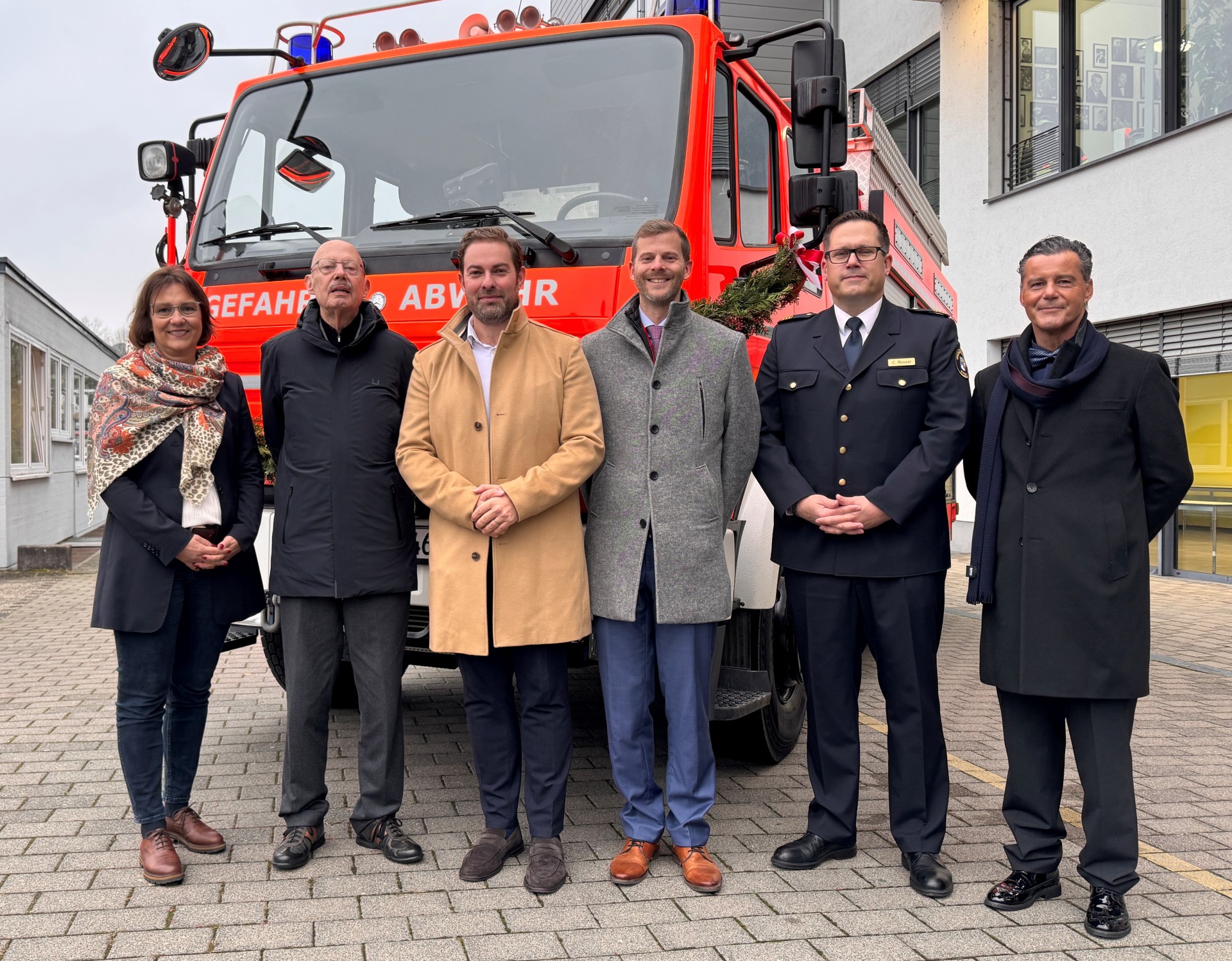 Vor einem Feuerwehrauto stehen vier Männer und eine Frau im Halbkreis. Alle tragen Winterjacken.