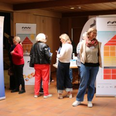 Ein Eingangsbereich mit Holzschiebetüren mit mehreren Personen und einem Banner der Polizei und ein weiterer Stand mit Pult und Bannern und einer Beachflag mit Webrung für Netzwerk Wohnen.