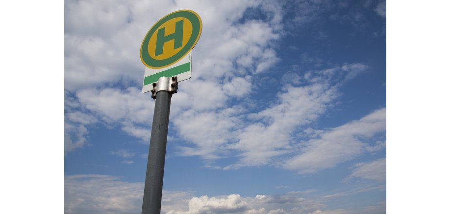 Schild mit grünem H auf gelben Kreis mit Blick in den blauen Himmel mit weißen Wolken