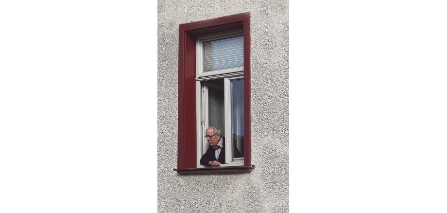 Alter Mann mit Brille schaut aus einem geöffnetem Fenster