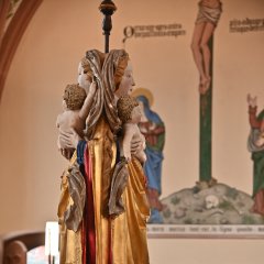 Eine Doppelmadonna, am Rücken gespiegelt hängt in der Michaelskapelle. Die Mariafigur mit langen blonden lockigen Haaren und einem braunen Tuch über den Haaren und einem gold-rotem Gewand hat das nackte Jesusbaby mit gelocktem Haar im Arm. Im Hintergrund das Kreuz Jesu, man sieht seine genagelten Beine und das Lendentuch und einen Totenkopf am Fusse des Kreuzes auf dem grauen Hügel. Danaben sind zwei Figuren. Unterhalb sind Besucher mit Corona-Masken.