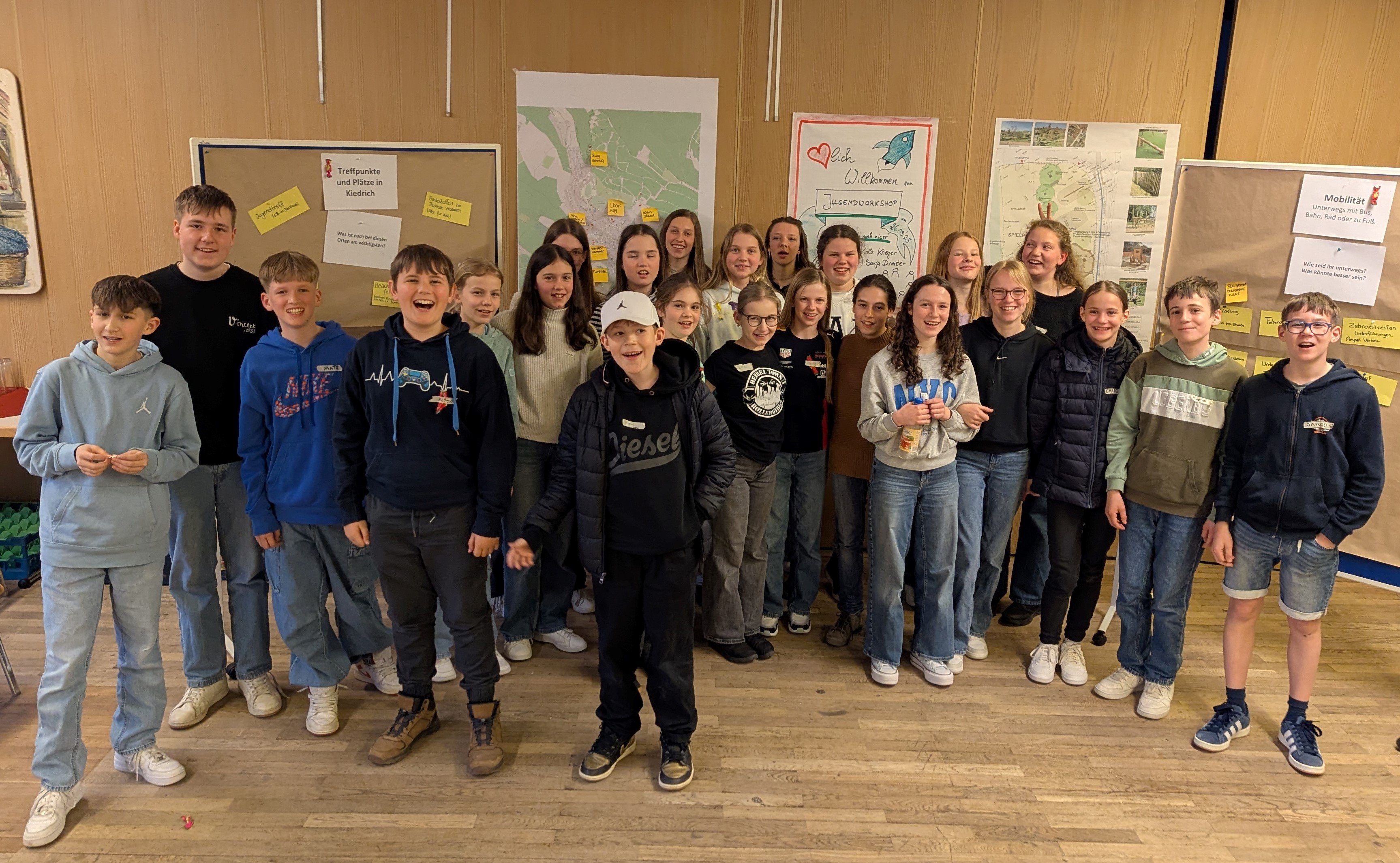 24 Kinder und Jugendliche stehen zusammen vor den erarbeiteten Pinwänden und Plakaten.  