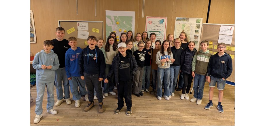 24 Kinder und Jugendliche stehen zusammen vor den erarbeiteten Pinwänden und Plakaten.  