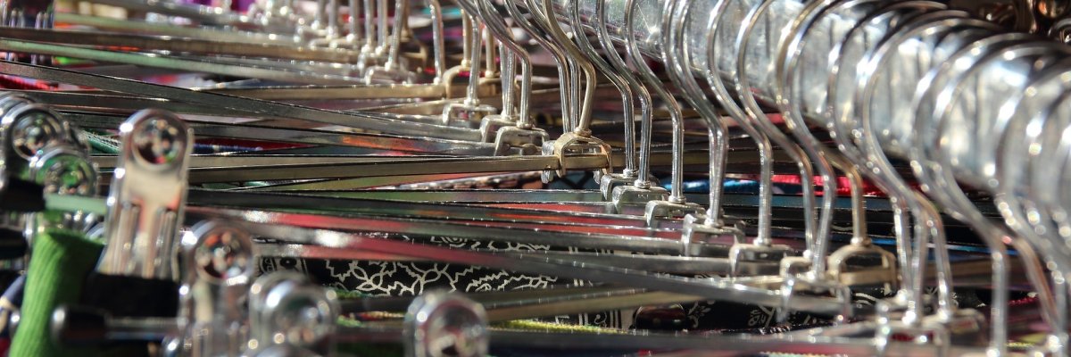 Eine Kleiderstange mit vielen Metall-Kleiderbügeln mit Klammern, an denen bunte Kleidung befestigt ist.