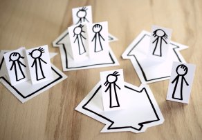 schwarze Strichmännchen und Häuser auf weißem Papier auf einem Holzuntergrund 