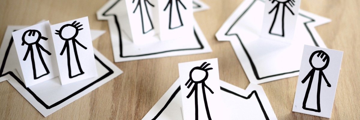 schwarze Strichmännchen und Häuser auf weißem Papier auf einem Holzuntergrund 